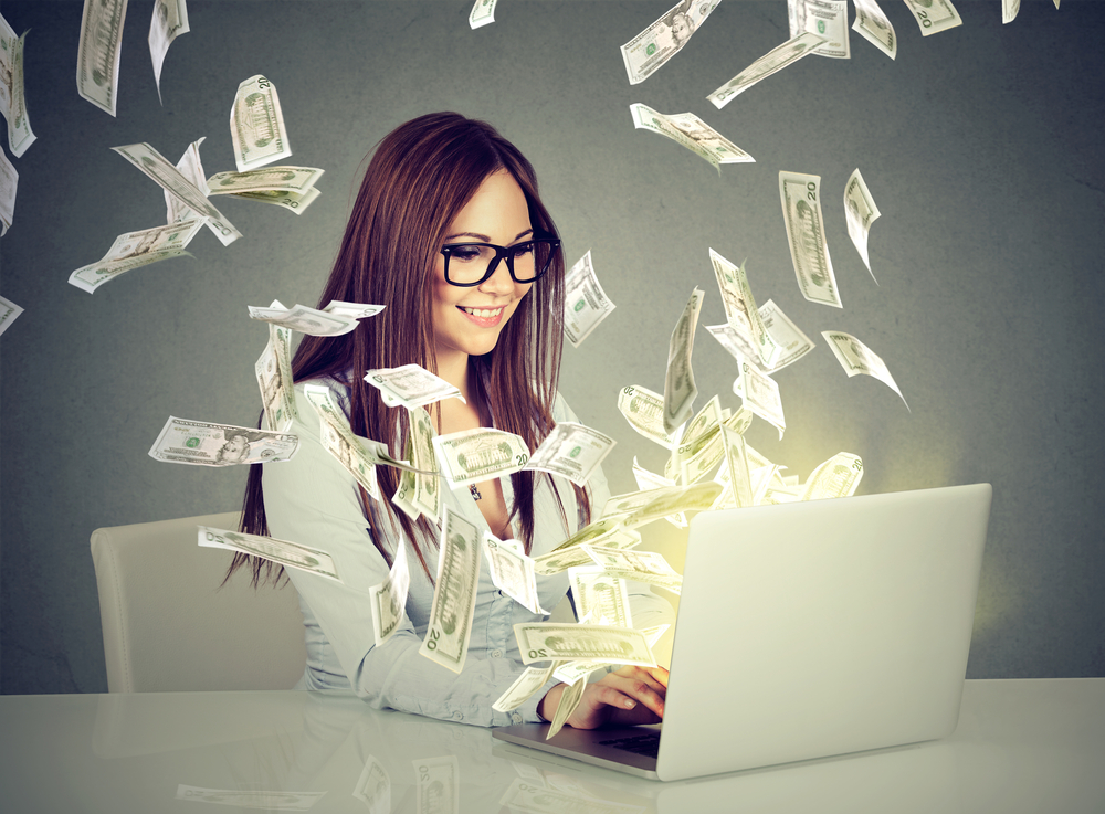 Person working on a laptop with money notes flying around