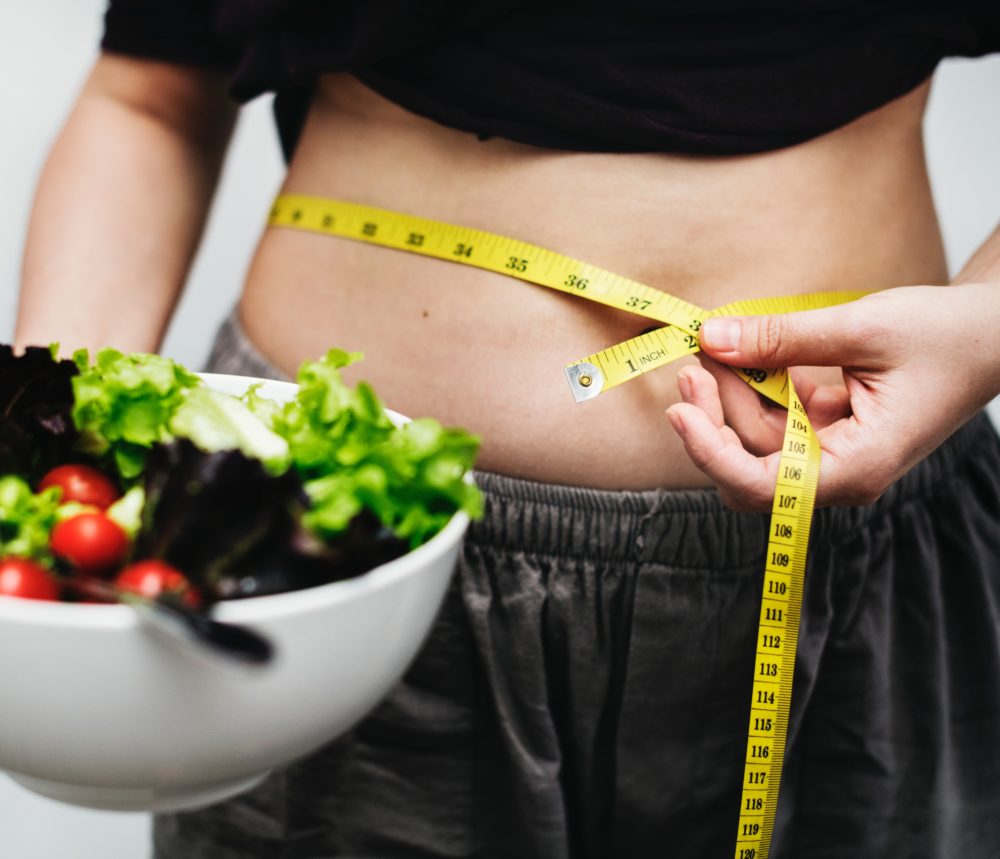 Person holding a salad and measuring their waist with a measuring tape