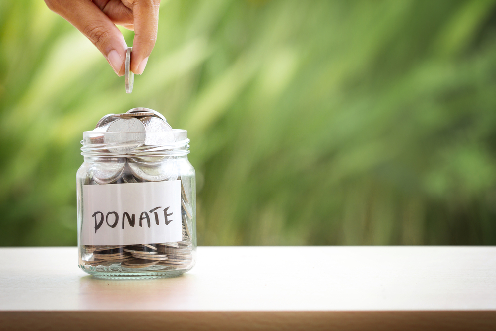 Person adding coins to donate jar – fundraising Person adding coins to donate jar - fundraising