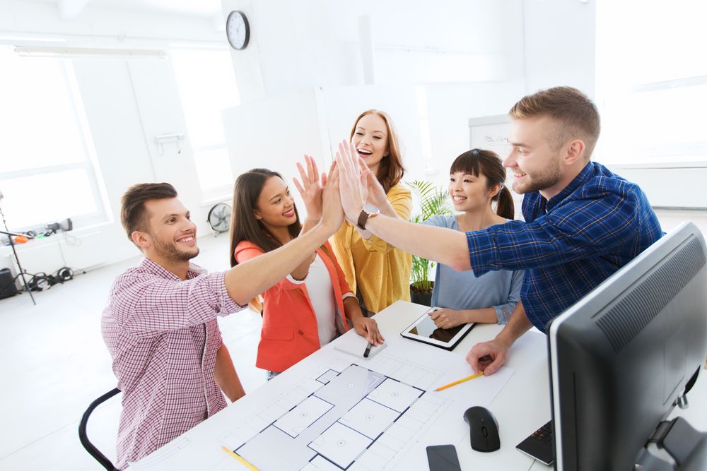 People high fiving over a computer and desk